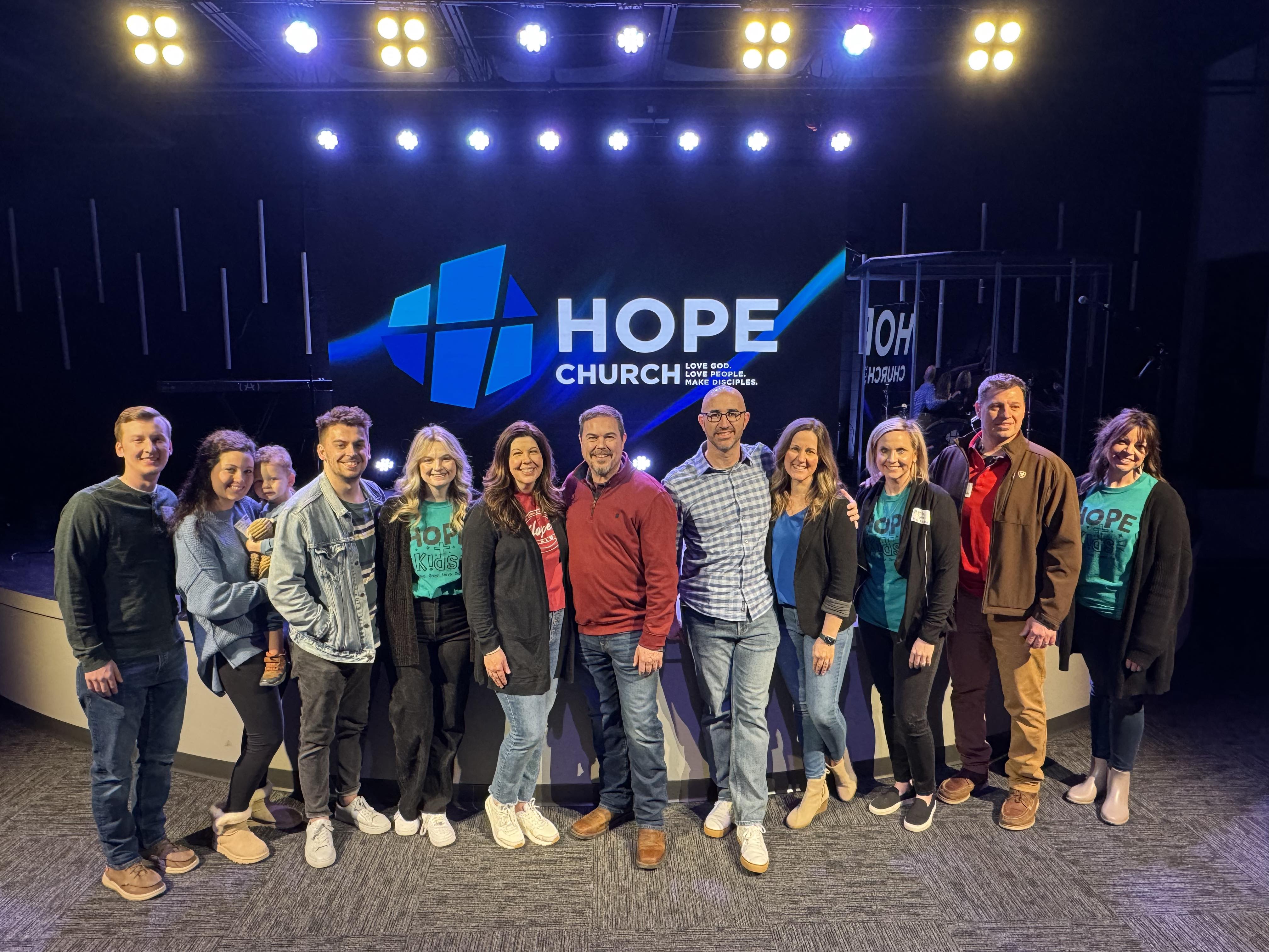 The Hope Church leadership team standing together on stage in front of the Hope Church logo