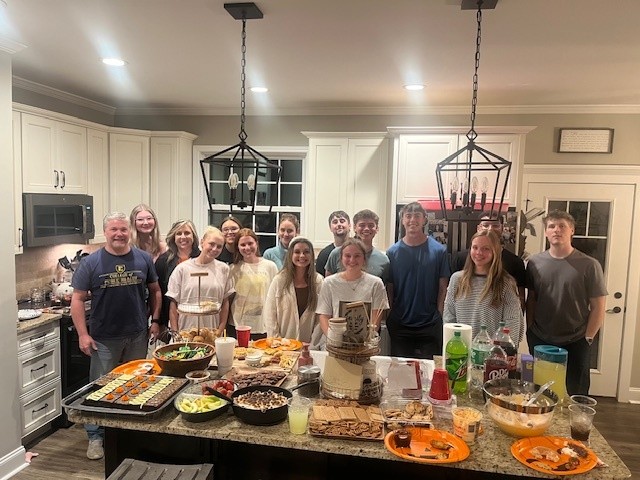 The College and Career group gathered around a kitchen island filled with food at a host home