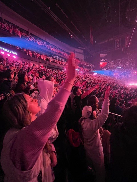 The Passion 2025 crowd with hands raised in worship under bright pink stage lights